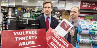 Two men are holding red signs that read "Violence threats abuse"