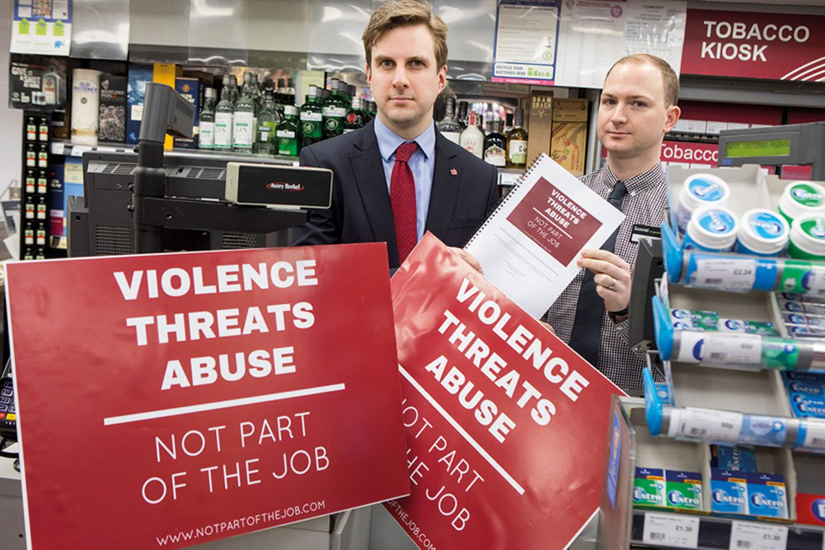 Two men are holding red signs that read "Violence threats abuse" 