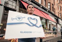 A man hold a large loves local gift card outside a store front