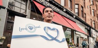 A man hold a large loves local gift card outside a store front