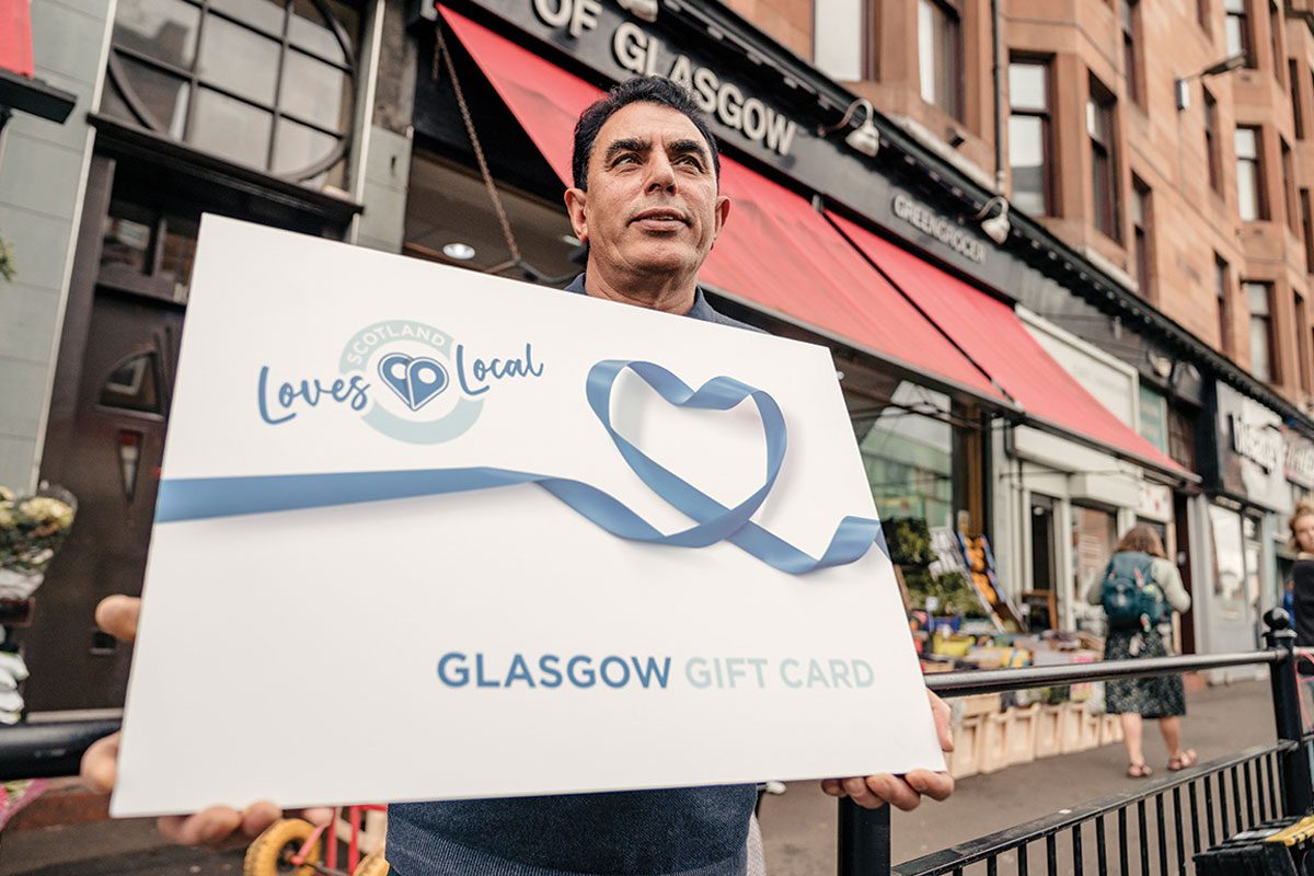 A man hold a large loves local gift card outside a store front