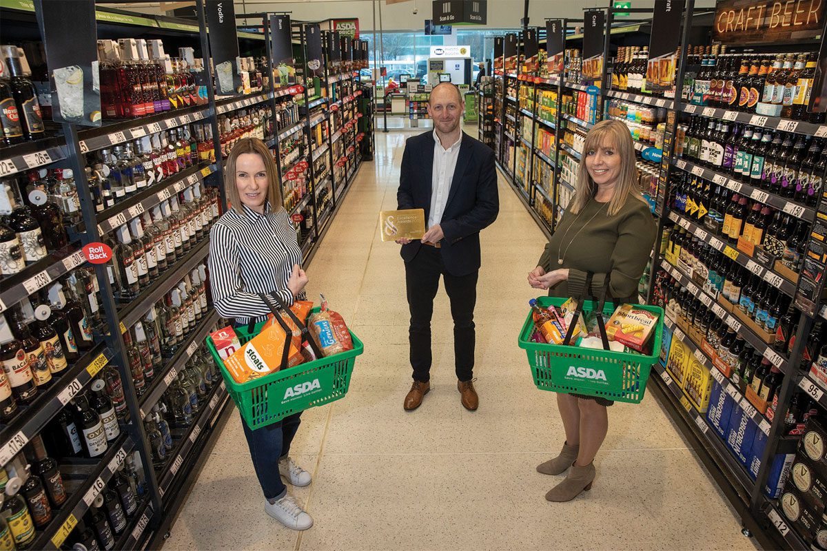 Three people stand in a supermarket aisle with baskets of scottish products