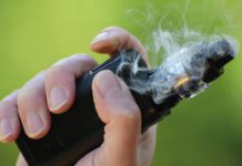 Hand holding a vape with green background
