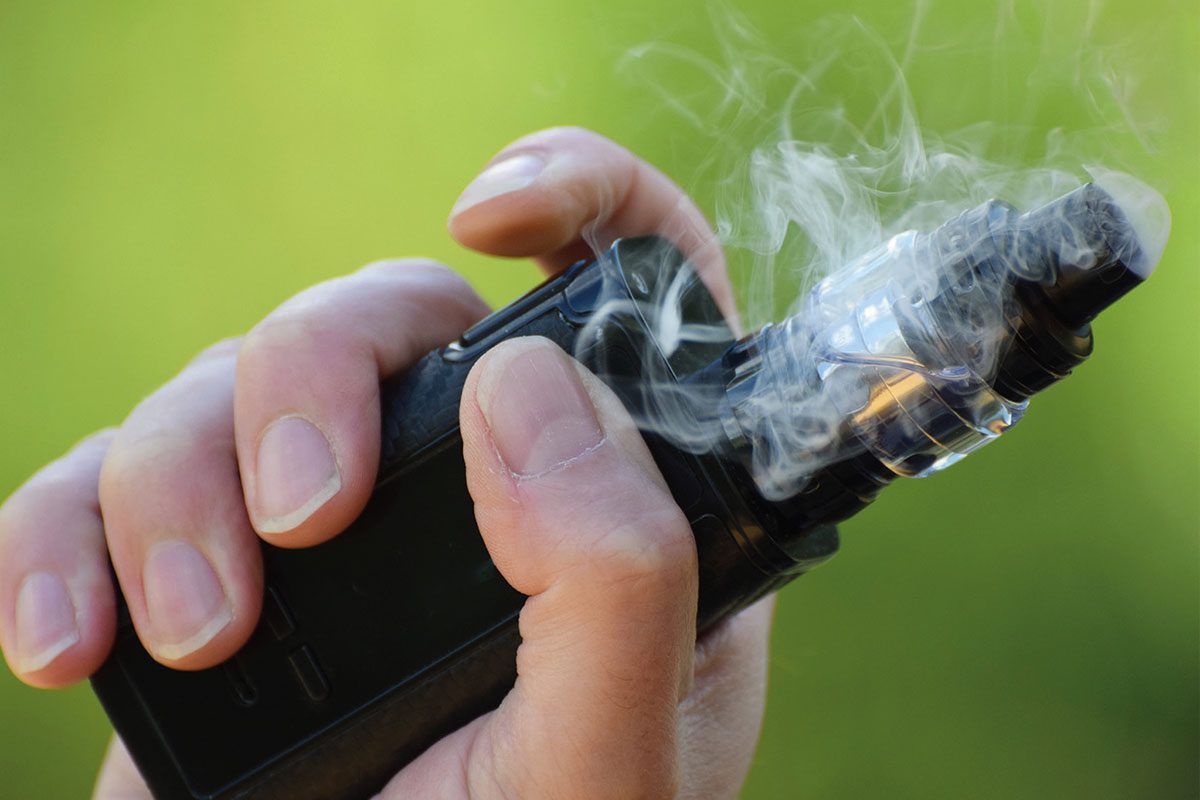 Hand holding a vape with green background