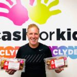 Innovative fundraising George bowie holds packets of mcghees cakes infront of cash for kids sign