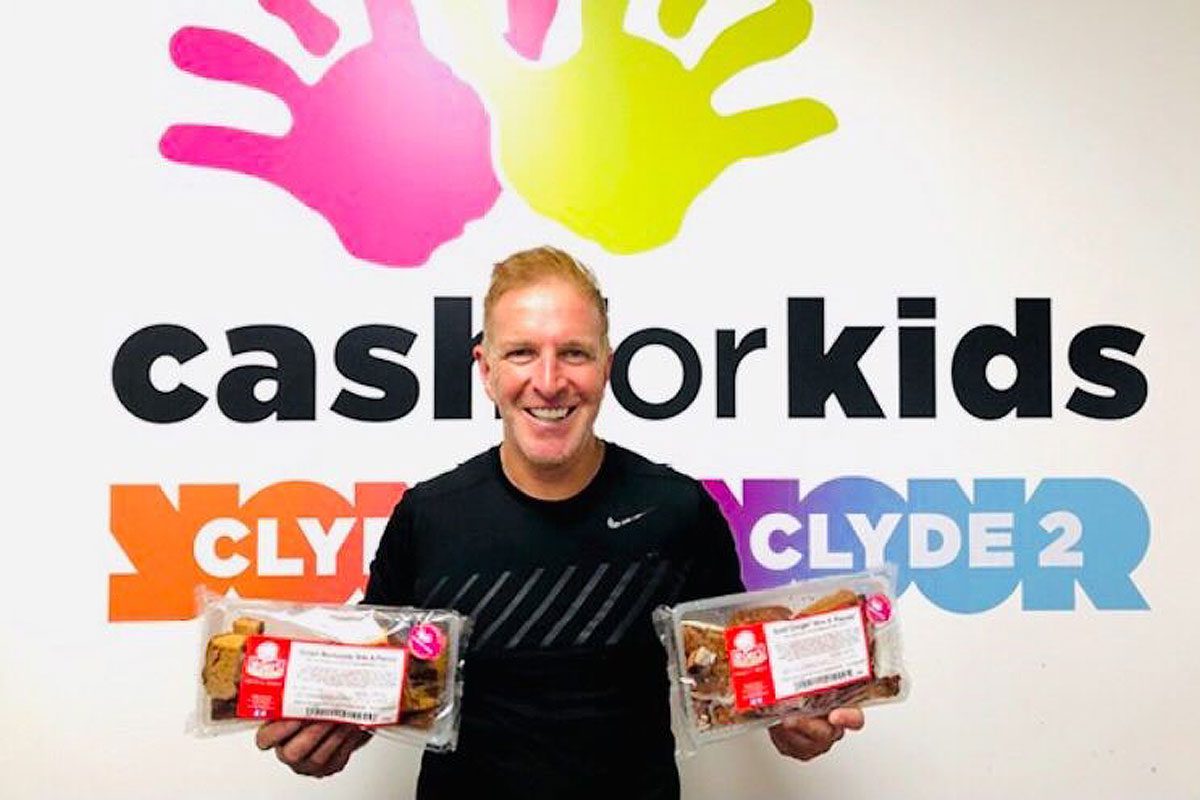 George bowie holds packets of mcghees cakes infront of cash for kids sign