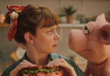 woman holding sandwich looking into a pig puppets eyes
