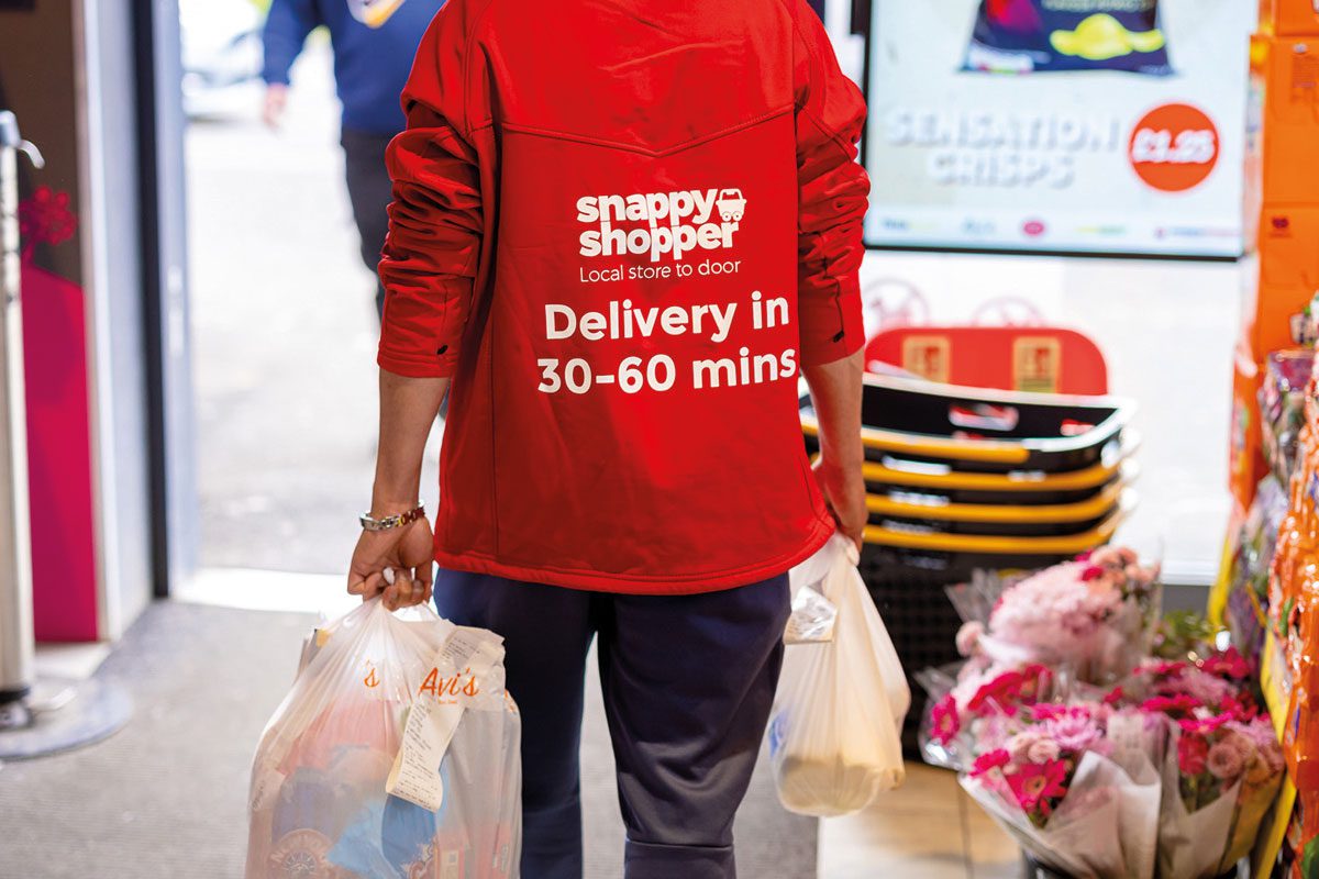 a snappy shopper deliver person carries two shopping bags out of a store
