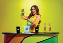 a woman holds a bottle of VK alcopop in a neon yellow dress infront of a neon yellow background