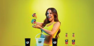 a woman holds a bottle of VK alcopop in a neon yellow dress infront of a neon yellow background