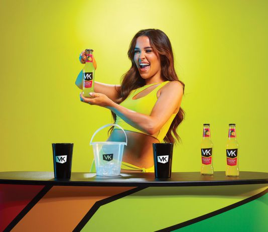 Vibrant new VK packaging a woman holds a bottle of VK alcopop in a neon yellow dress infront of a neon yellow background