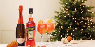 A bottle of aperol spritz and prosecco next to two aperol spritz cocktails and canopes