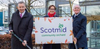 Three people hold a sign for Scotmid community orchard