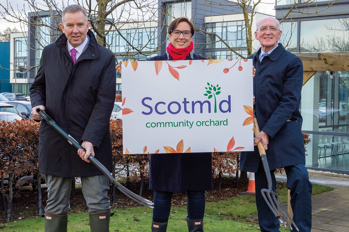Three people hold a sign for Scotmid community orchard