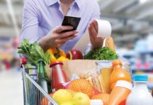 A shopper pushes a trolley full of groceries with holding a mobile phone