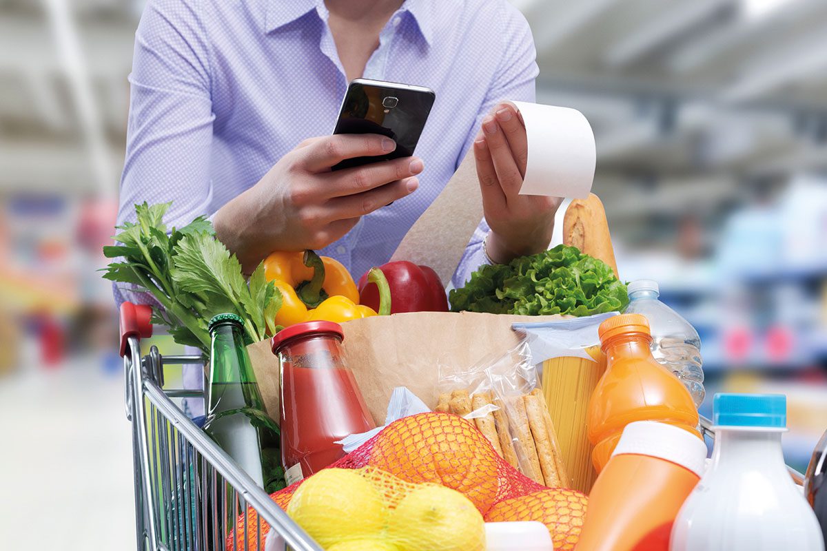 A shopper pushes a trolley full of groceries with holding a mobile phone