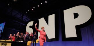 Nicola Sturgeon walking across stage with SNP in large letters