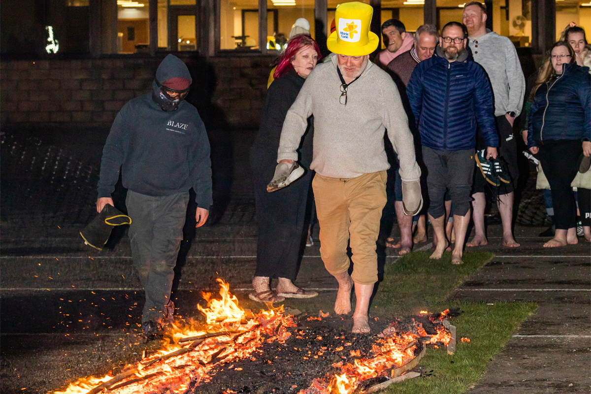 Spar Scotland colleague walking across fire with a Marie Curie hat on