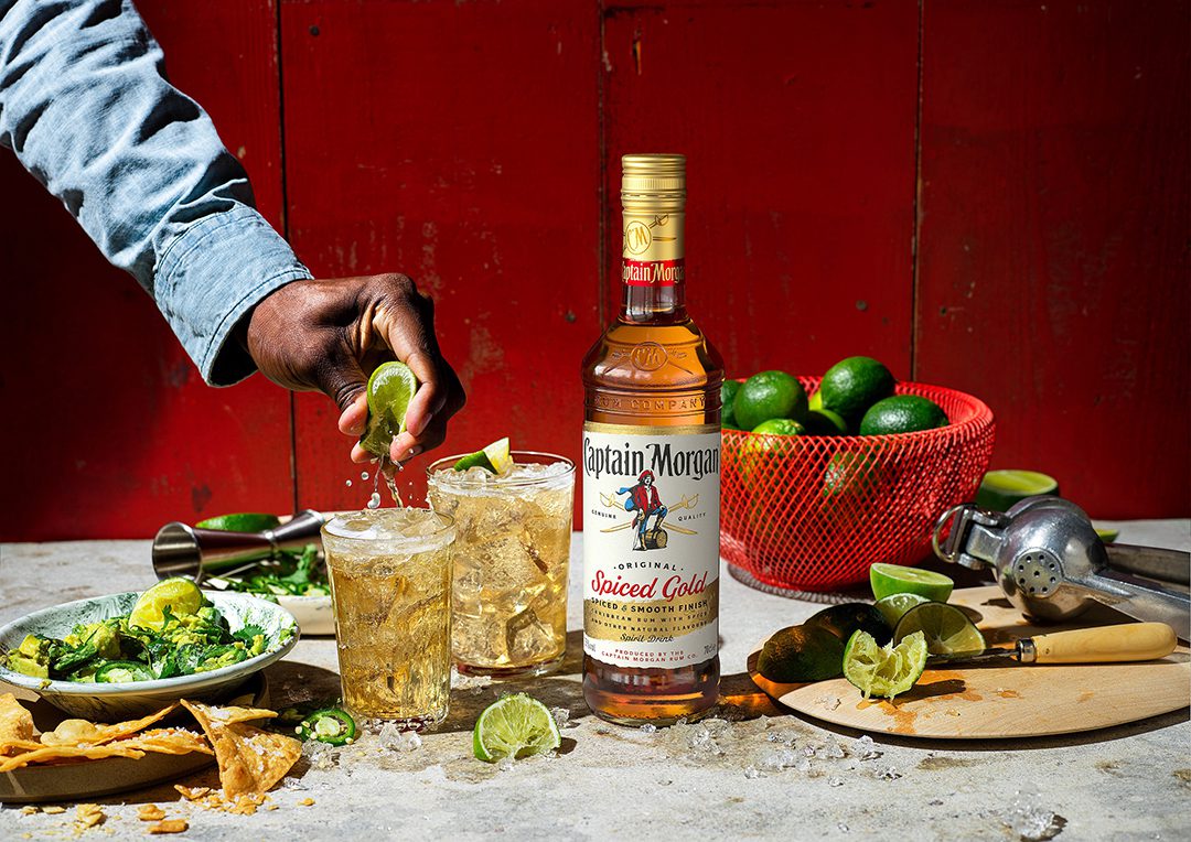 A man squeezing a lime into a drink containing Captain Morgan Spiced Rum which also features the brand's new design.