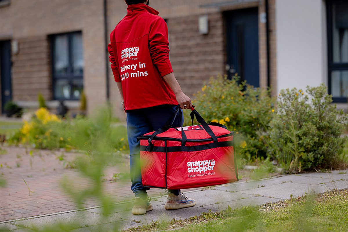 Snappy Shopper delivery driver making a delivery to a local house with a red Snappy Shopper branded bag.