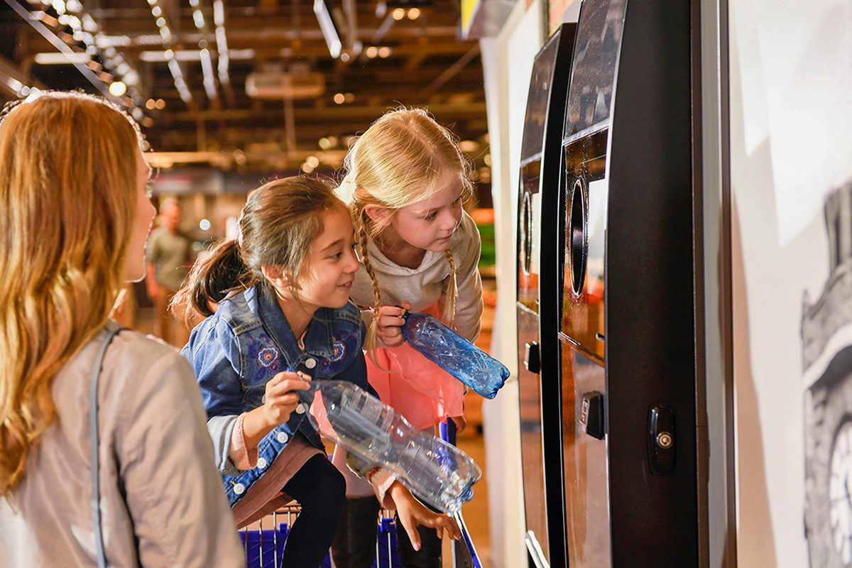 Children looking into a reverse vending machine with plastic bottles in their hands ready to recycle them.