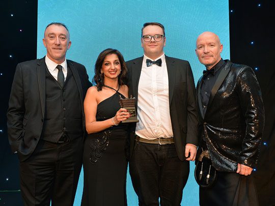 (From left to right) John Leslie, customer development manager at Britvic, Shamly Sud, director at GHSL, the former manager of Premier Racetrack Pitstop Bearsden and Craig Hill, comedian and host of the Scottish Grocer Awards 2022, stand together as Premier Racetrack Pitstop Bearsden receives the Sustainability Champion award.