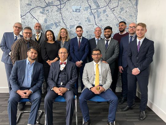 A group of Forum Insurance employees pose together for a group photo against a map of London.