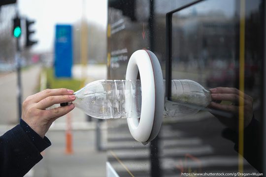 Someone places a plastic bottle into a reverse vending machine ti recycle it.
