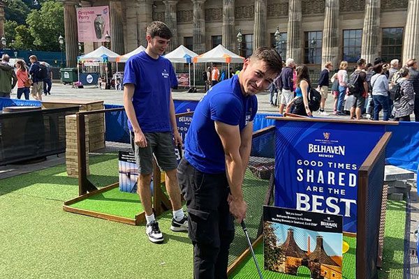 Two people stand playing mini golf at Belhaven Brewery's new course at its Edinburgh Fringe Festival pop-up bar, Belhaven Bar on the Mound.