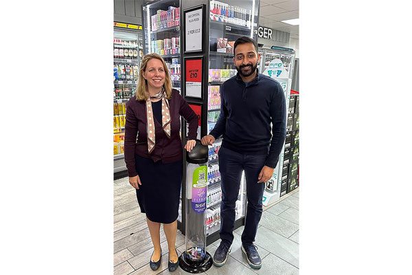 (Left to right) Eve Peters and Anand Cheema stand in a convenience store with their hands sitting on top of a disposable vape recycling bins.