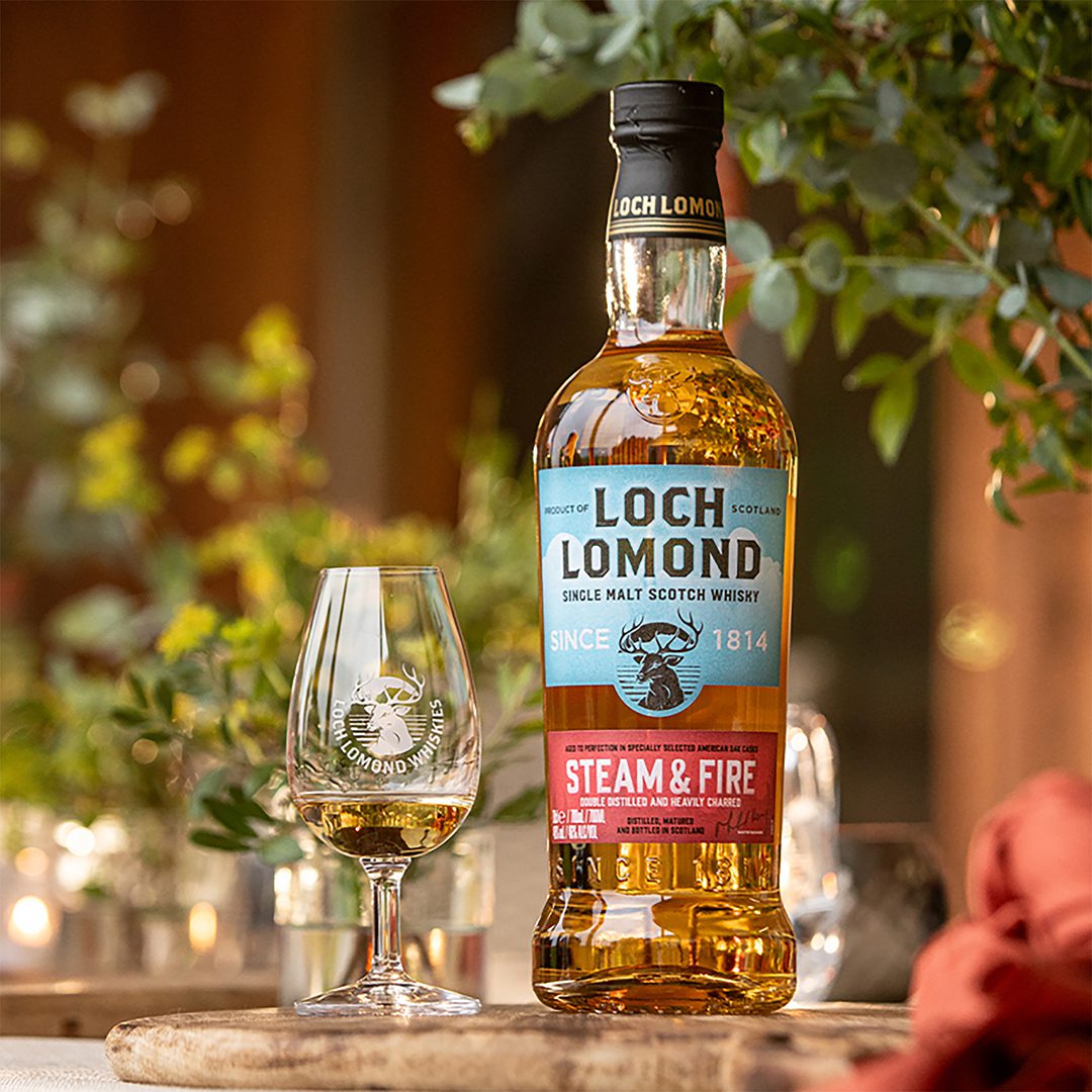 A bottle of the new Steam & Fire whisky from Loch Lomond Distilleries stands on a table with a dram next to it.