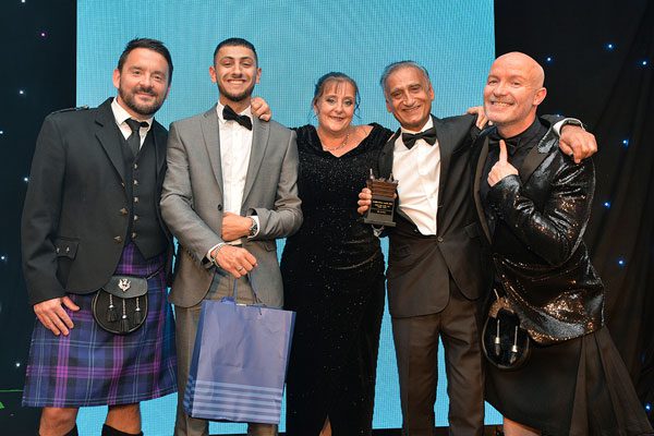 Five people stand on a stage in formal attire as the three members in the middle accept the Symbol Store of the Year (Single) Award.