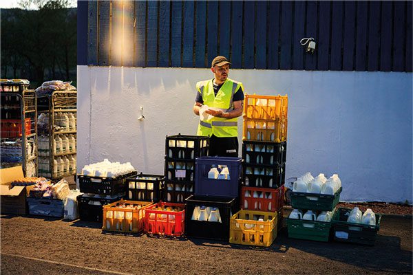 A man stands among plastic crates with milk cartons in them.