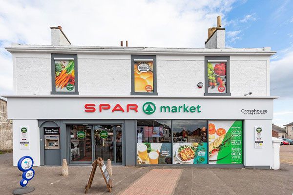 Store front shot of Spar Market Crosshouse; a white building with Spar Market branding above its door with windows advertising fresh food products.