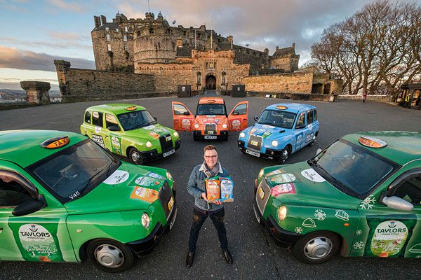 Greg Smith, head of marketing at Taylors Snacks, stands in front of Edinburgh Castle with taxis surrounding him wrapped in different colours to advertise different variants of Taylors Snacks crisps.