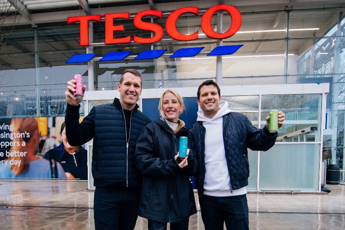 Three people stand in front of a Tesco store front holding cans of Served cocktails.