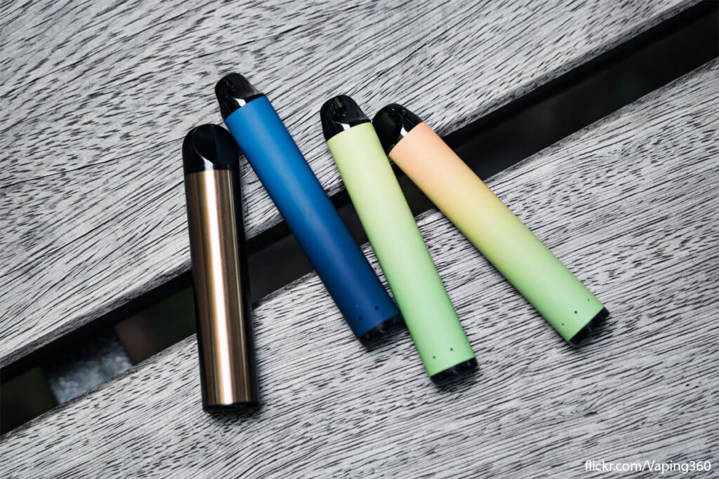 Disposable vape devices sit on a wooden bench in an array of colours.