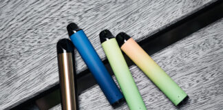 Disposable vape devices sit on a wooden bench in an array of colours.