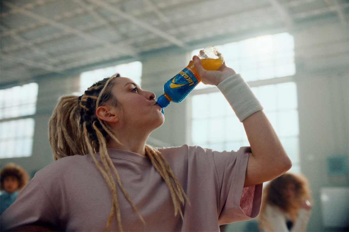 A woman taking an exercise class drinks from a bottle of Lucozade Sport featuring the new design.