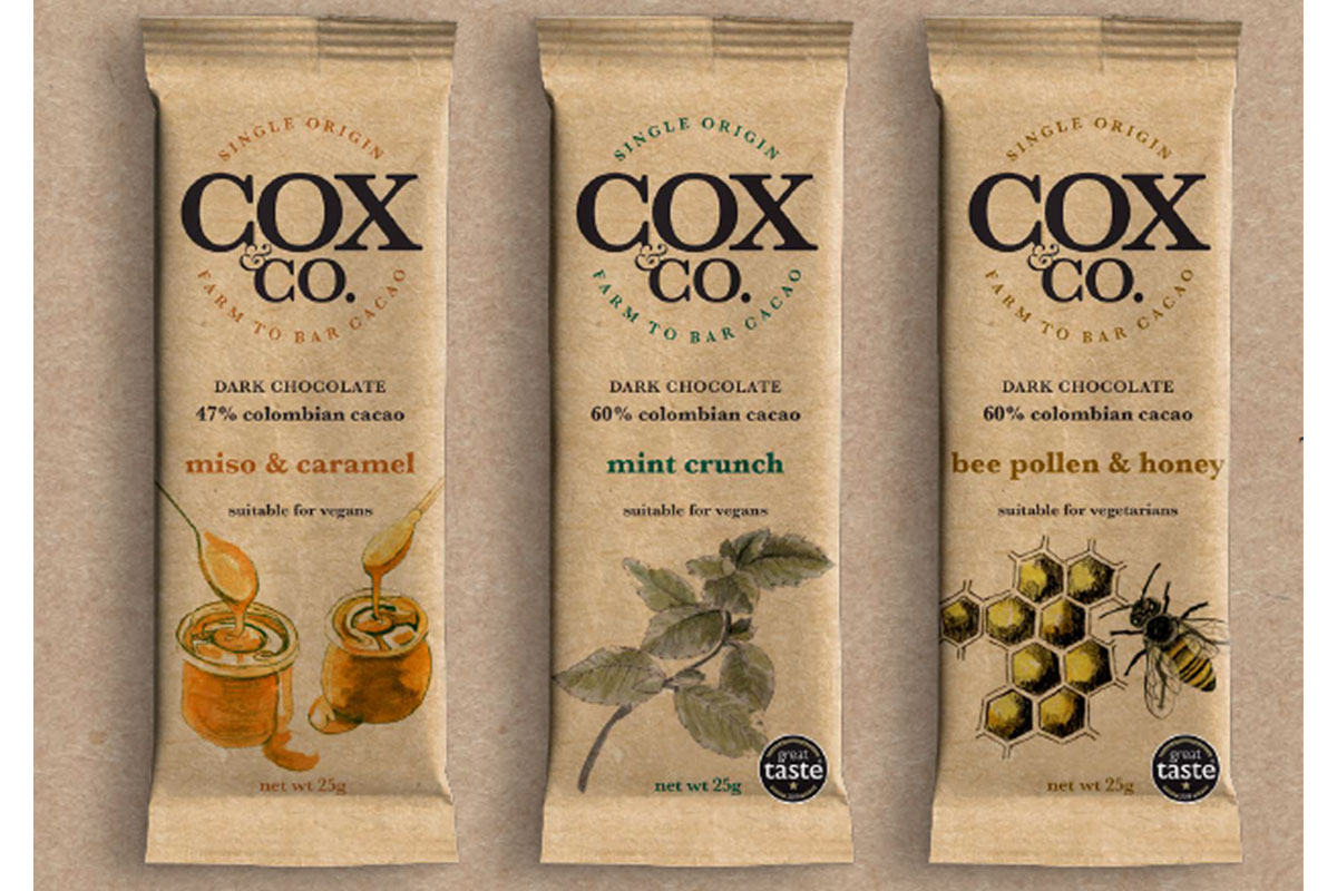 Packs of the new flow paper packaging for Cox & Co chocolate lie against a paper background.