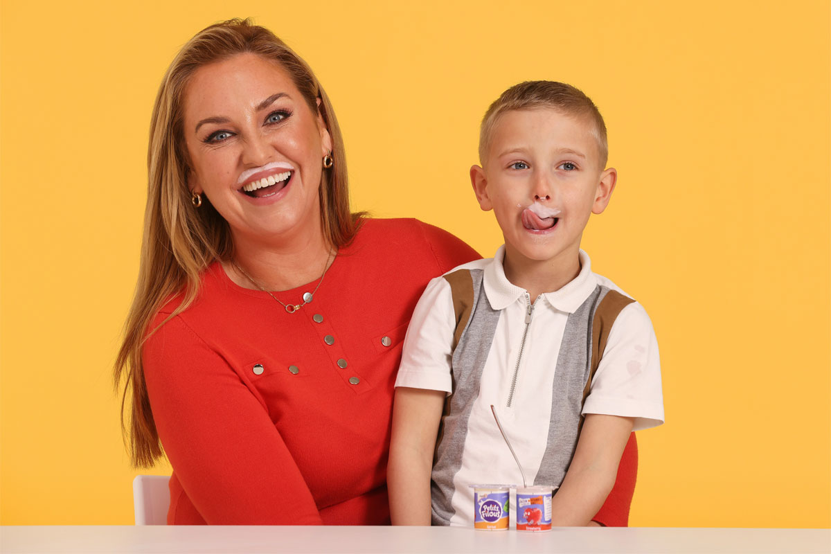 Josie Gibson and her son Reggie sit against a yellow background smiling with yoghurt moustaches as part of the new campaign for Yoplait.