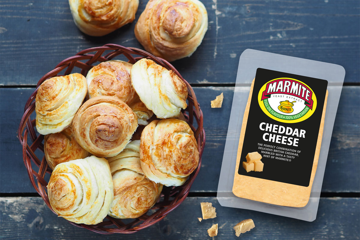 A basket of pinwheels sits next to a packet of Marmite Cheddar Cheese on a wooden table.