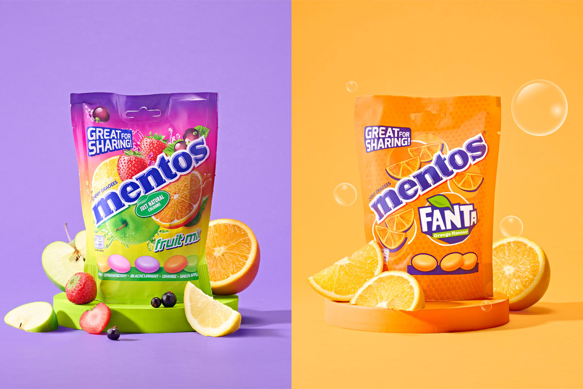 Promotional image of the new Mentos Sharing Packs with the Fruit Mix variant to the left surrounded by fruit against a purple background and the Fanta variant to the right surrounded by oranges and bubbles against an orange background.