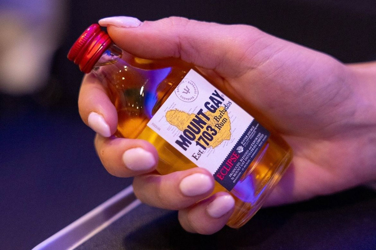 A hand holds a small 50ml bottle of Mount Gay Eclipse rum onboard an airplane.