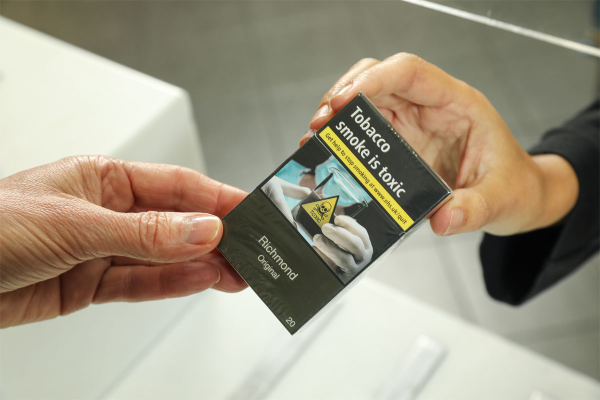 A person hands somebody else a packet of cigarettes with a health warning seen on the pack.