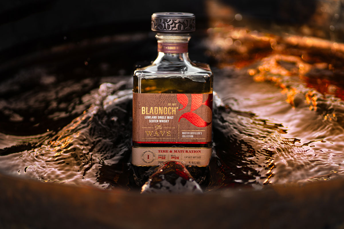 A bottle of Bladnoch The Wave whisky sits in the middle of a stream of water which parts around the bottle.