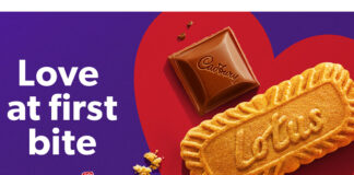 Promotional image for the team up of Cadbury and Lotus Bakeries with a piece of Cadbury Dairy Milk chocolate and a Lotus biscuit side by side in a red love heart with text on the left reading 'Love at first bite'.