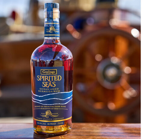 New Goslings Rum docks in the UK A bottle of Goslings Spirited Sea sits on a wooden bannister of a ship with a ship's wheel blurred in the background.