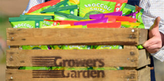 A person carrying a wooden crate with the Growers Garden logo burned on to it with packs of Broccoli Chips inside the crate.