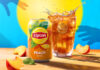 A can of Lipton Iced Tea sits next to a glass filled with the drink with peach pieces around them. There is also a blue background with yellow sun and silhouetted hands reaching for the drink.